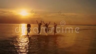 一群快乐的女孩在海滩上奔跑玩耍，在夕阳下跳舞，在夏天的夕阳下喷洒。 海滩